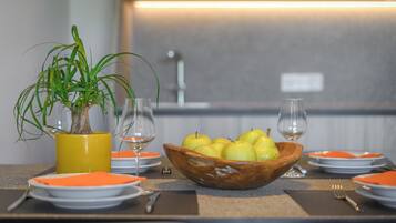 Una mesa de comedor con un cuenco de madera lleno de fruta, una planta en maceta y platos y cubiertos colocados cuidadosamente.