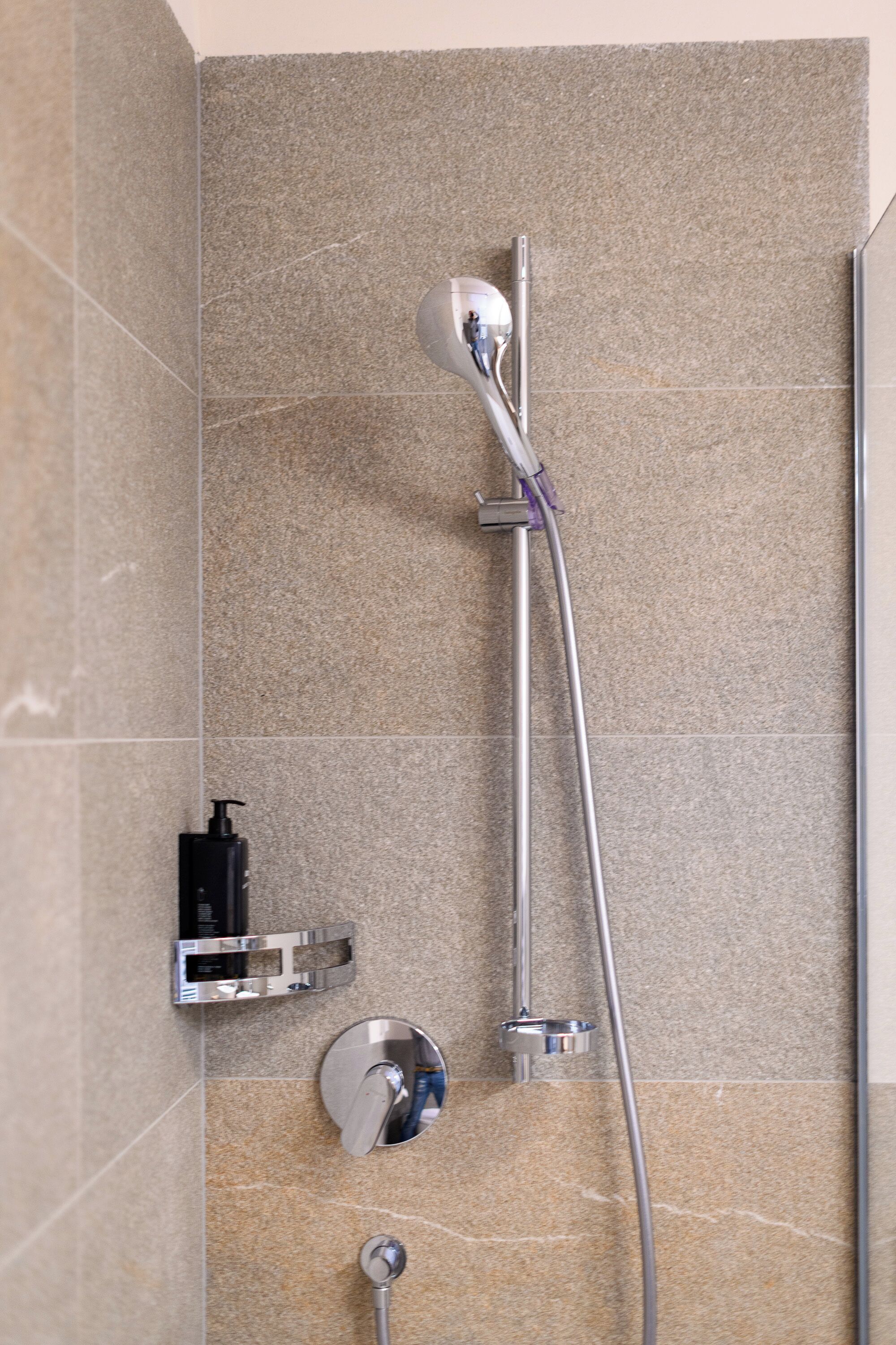 Ducha con cabezal de ducha de mano, grifo empotrado en la pared y dispensador de jabón.