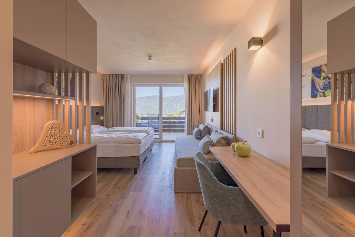 A modern hotel room with a balcony, a desk, two beds, and a TV.