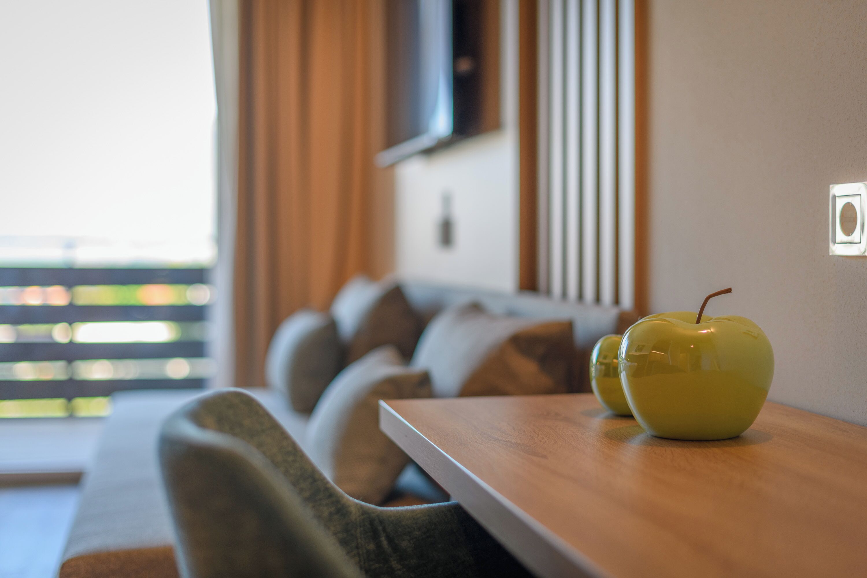 A modern living room with a wooden table, two green apples, a sofa, and a television mounted on the wall.