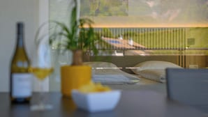 A room with a bed, a table with a bottle and glasses, and a view of a balcony with a railing.