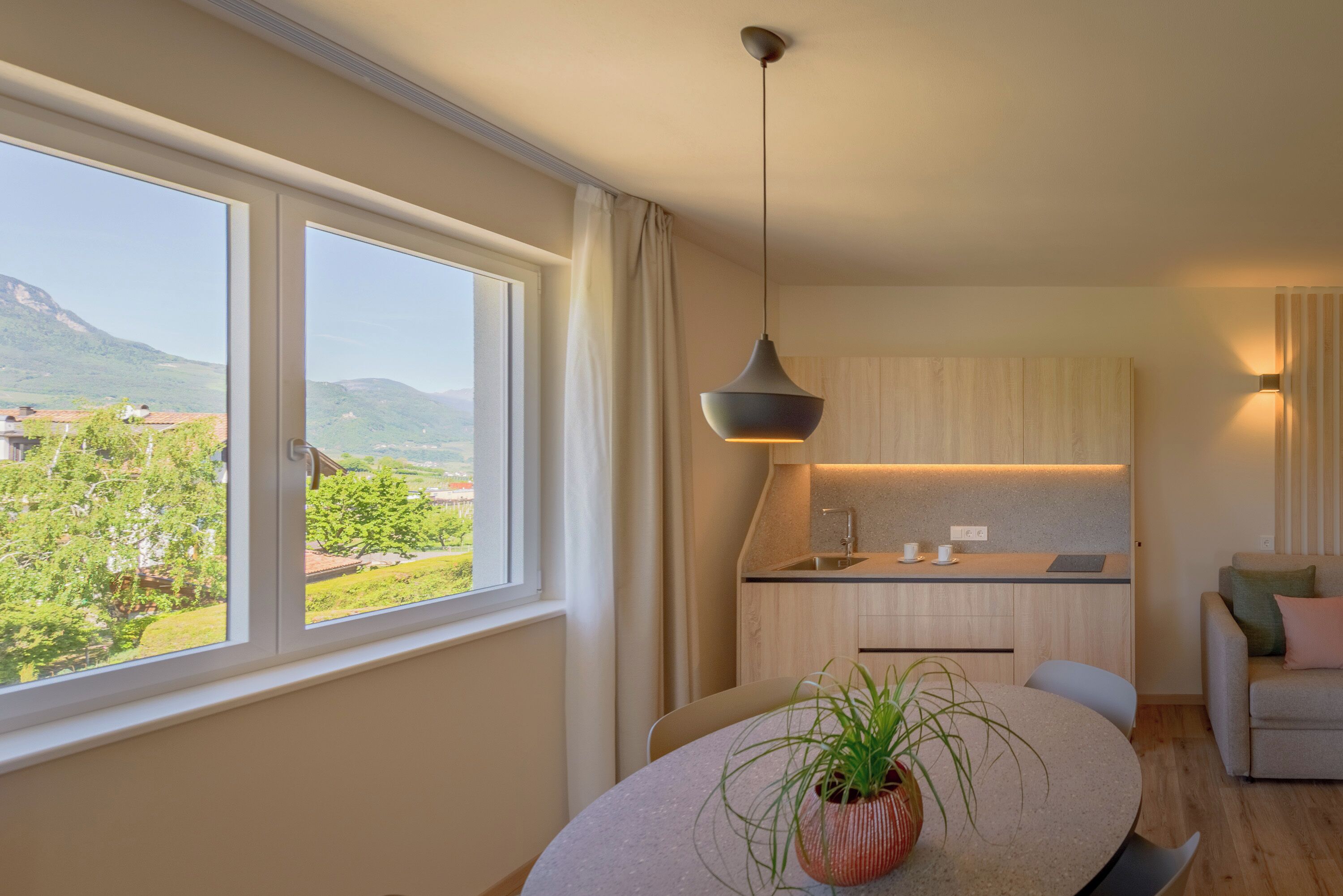 Une cuisine moderne offrant une vue sur un paysage montagneux, un coin repas avec une table et des chaises, et un canapé dans l’espace de vie.