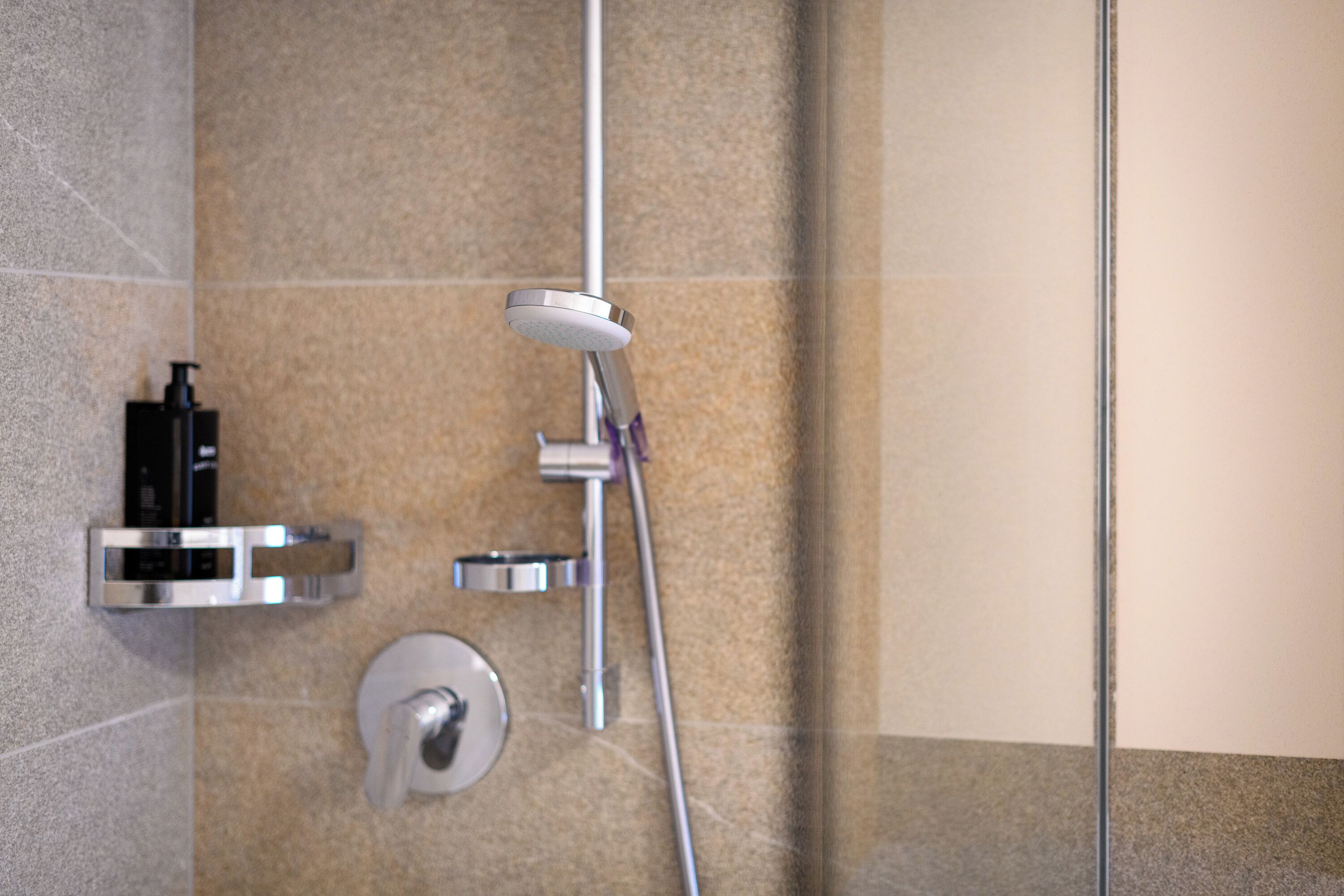 A modern shower with a handheld showerhead, a wall-mounted control panel, and a soap dispenser.