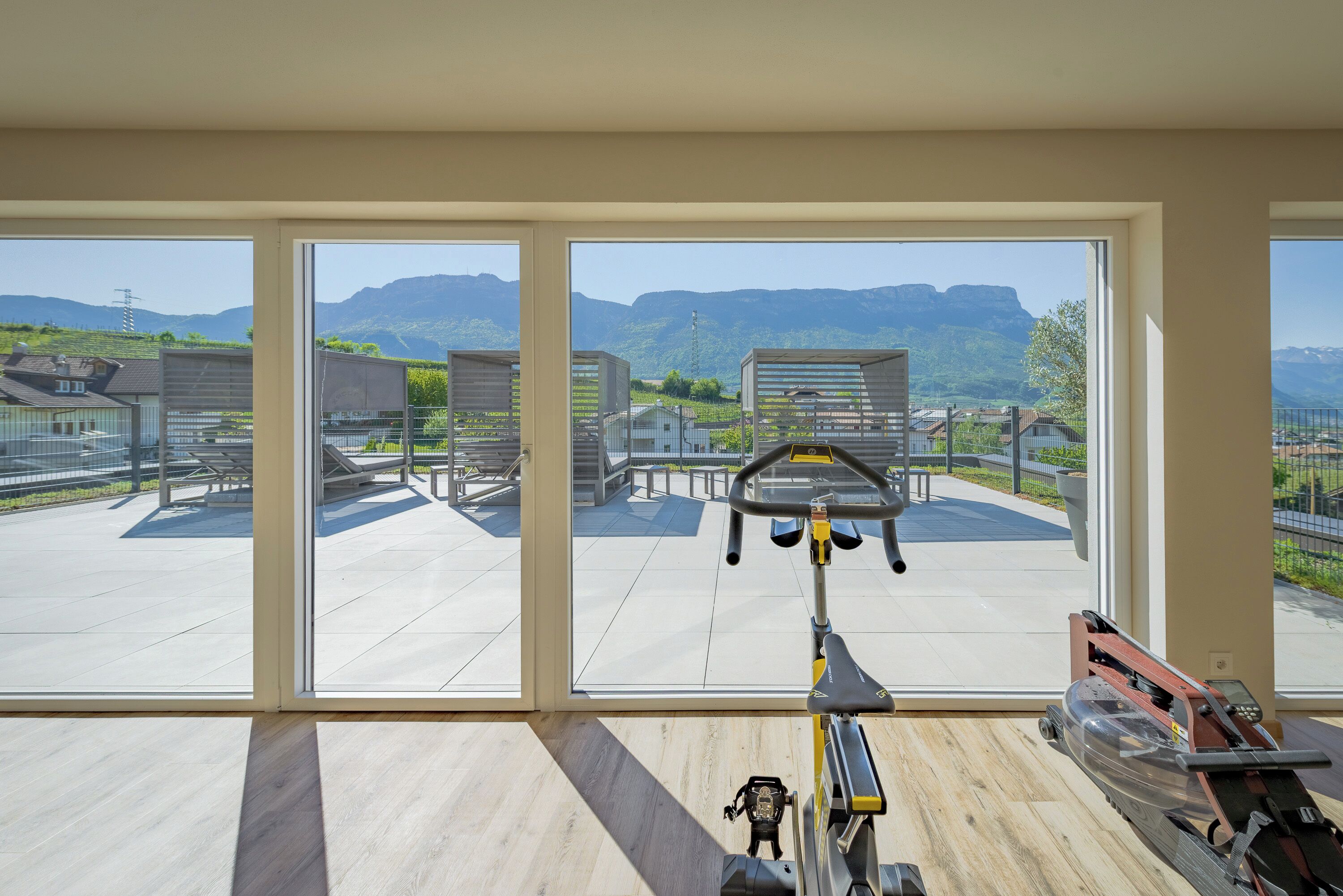 A spacious room with large windows offering a view of a mountainous landscape and a patio area with outdoor furniture.