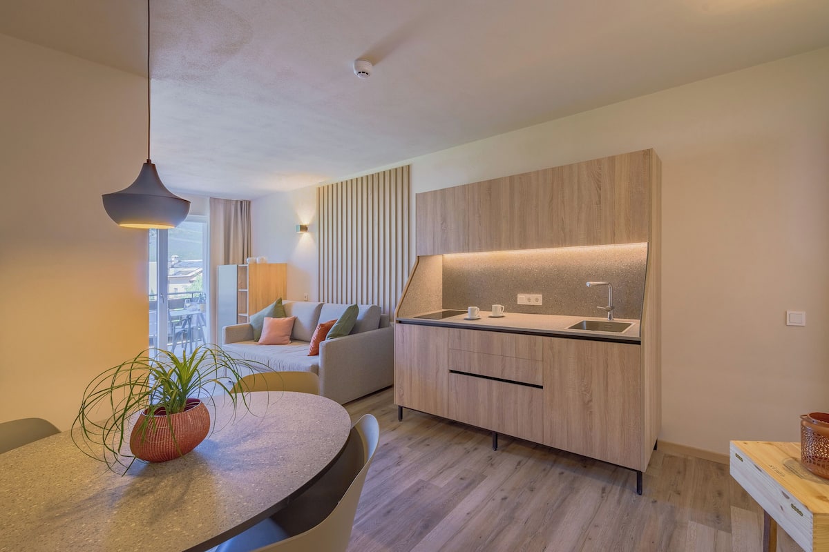A modern kitchen with a built-in oven, a dining area with a round table, and a sofa in the background.