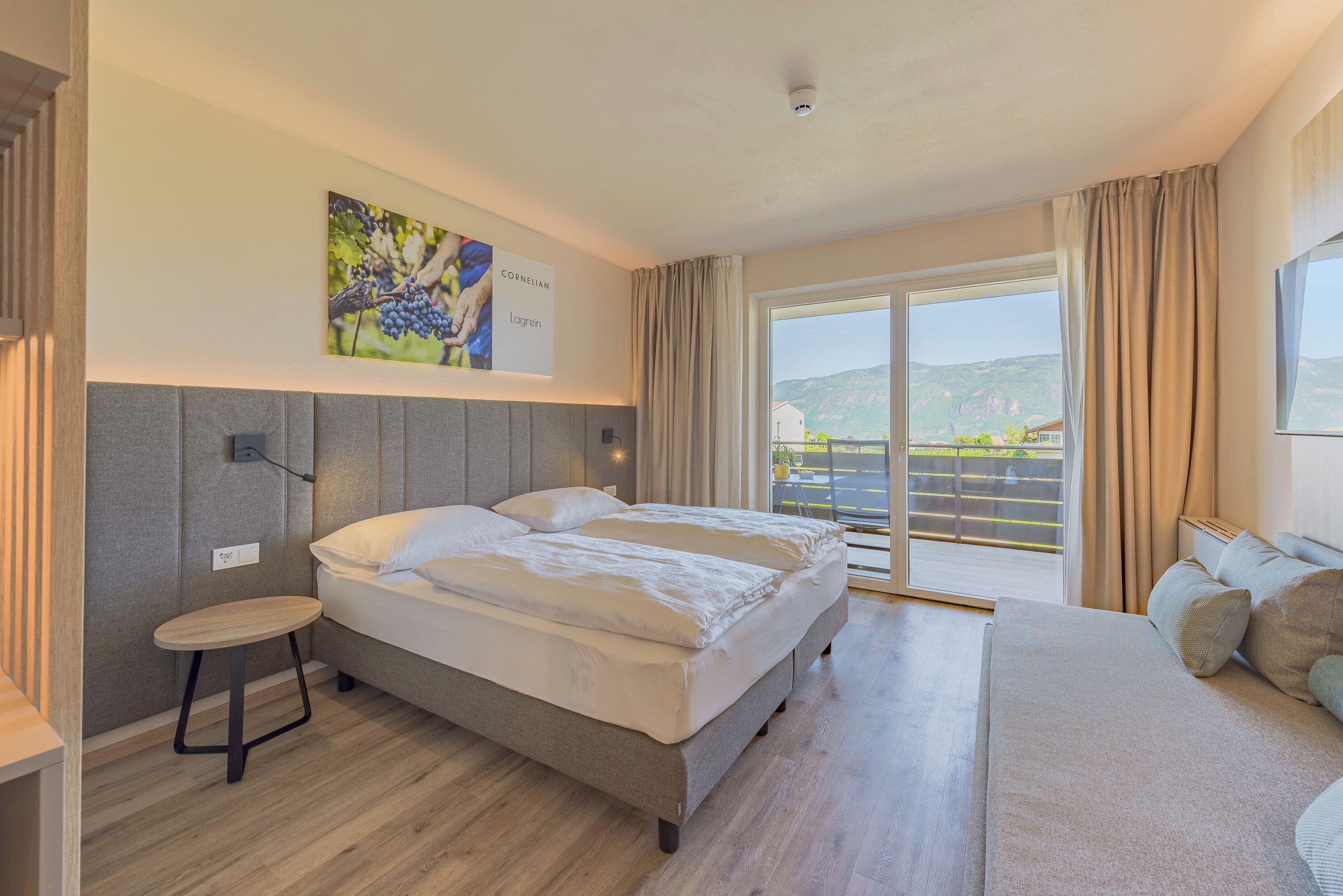 A modern hotel room with a bed, a small table, a sofa, and a large window with a view.