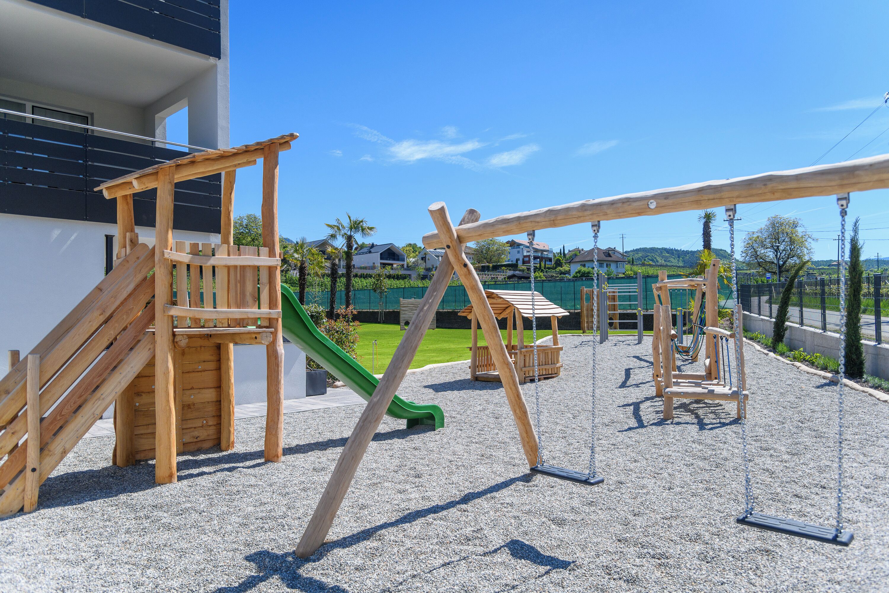 A playground with wooden structures, including a slide and swings, set against a residential backdrop.