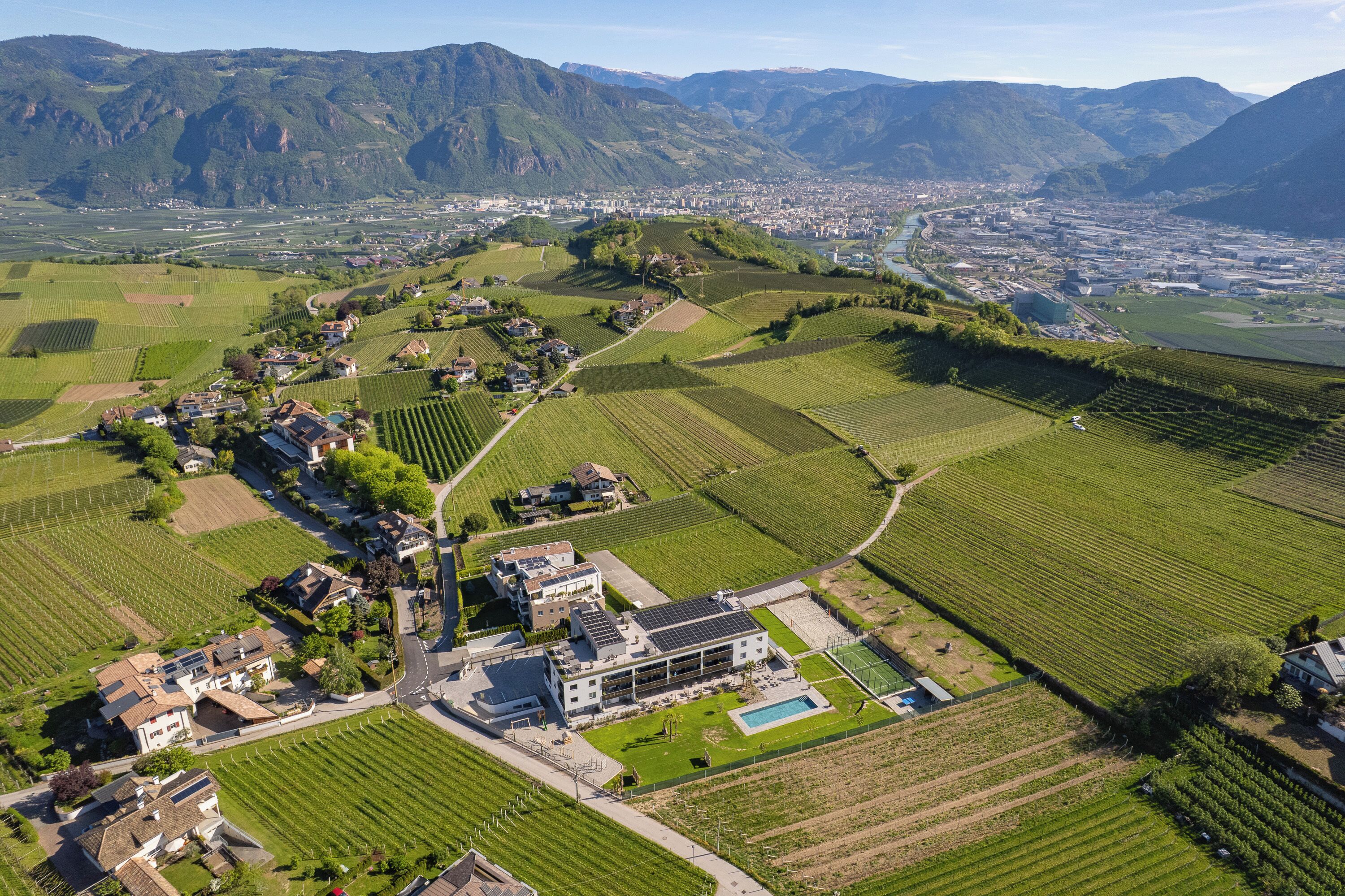 Paisaje rural con viñedos, piscina y un edificio moderno con paneles solares.