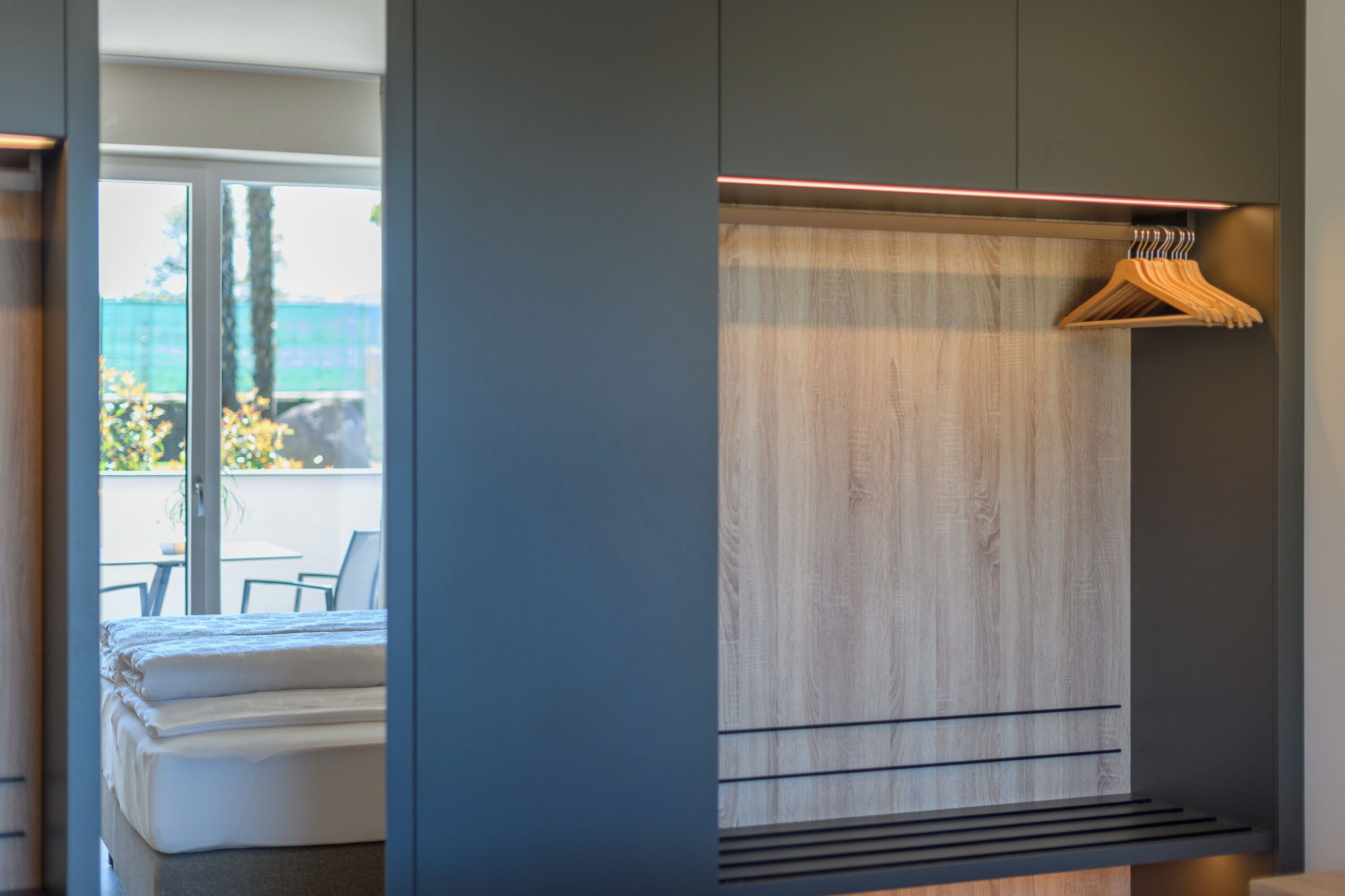 Une chambre à coucher moderne avec un lit, un mur recouvert de panneaux en bois, un porte-manteau en bois et une vue sur l’extérieur.