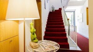 A hotel hallway with a red carpeted staircase, a round table with a lamp, and a red chair. - Haus am Mühlenweg (Bad Woerishofen)