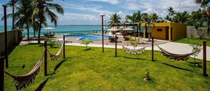 A pool area with a view of the ocean, a hammock, and a small building. - Beira Mar C Piscina e Area Gourmet 113D (Ipojuca)
