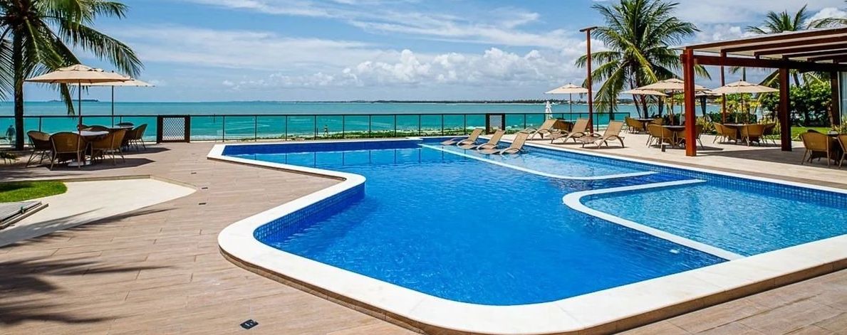 A pool area with lounge chairs and umbrellas, overlooking a beach.