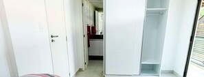 A narrow hallway with a door on the left, a closet on the right, and a glimpse of a kitchen area in the background. - Beira Mar C Piscina e Area Gourmet 113D (Ipojuca)