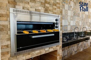 A kitchen with a built-in stainless steel oven, a sink, and a tiled backsplash. - Beira Mar C Piscina e Area Gourmet 113D (Ipojuca)