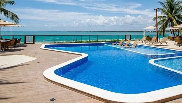 A pool area with lounge chairs and umbrellas, overlooking a beach. - Beira Mar C Piscina e Area Gourmet 113D (Ipojuca)