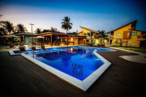 A pool area with lounge chairs and umbrellas, a sign that says "Stay Fall", and a building with a modern design. - Beira Mar C Piscina e Area Gourmet 113D (Ipojuca)