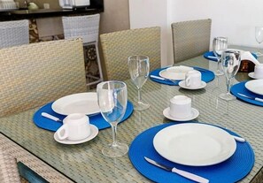 A dining table set with white plates, blue placemats, and clear glassware. - Beira Mar C Piscina e Area Gourmet 113D (Ipojuca)