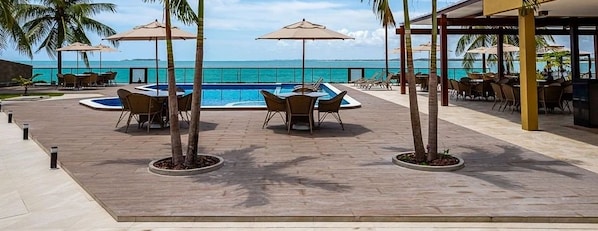 Ein Poolbereich mit Tischen und Stühlen und Blick aufs Meer.