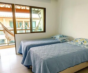 Quarto com duas camas, uma rede e vista para um prédio.