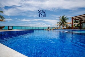 A swimming pool with lounge chairs and umbrellas, a clear sky, and a 'Stay' sign. - Beira Mar C Piscina e Area Gourmet 113D (Ipojuca)