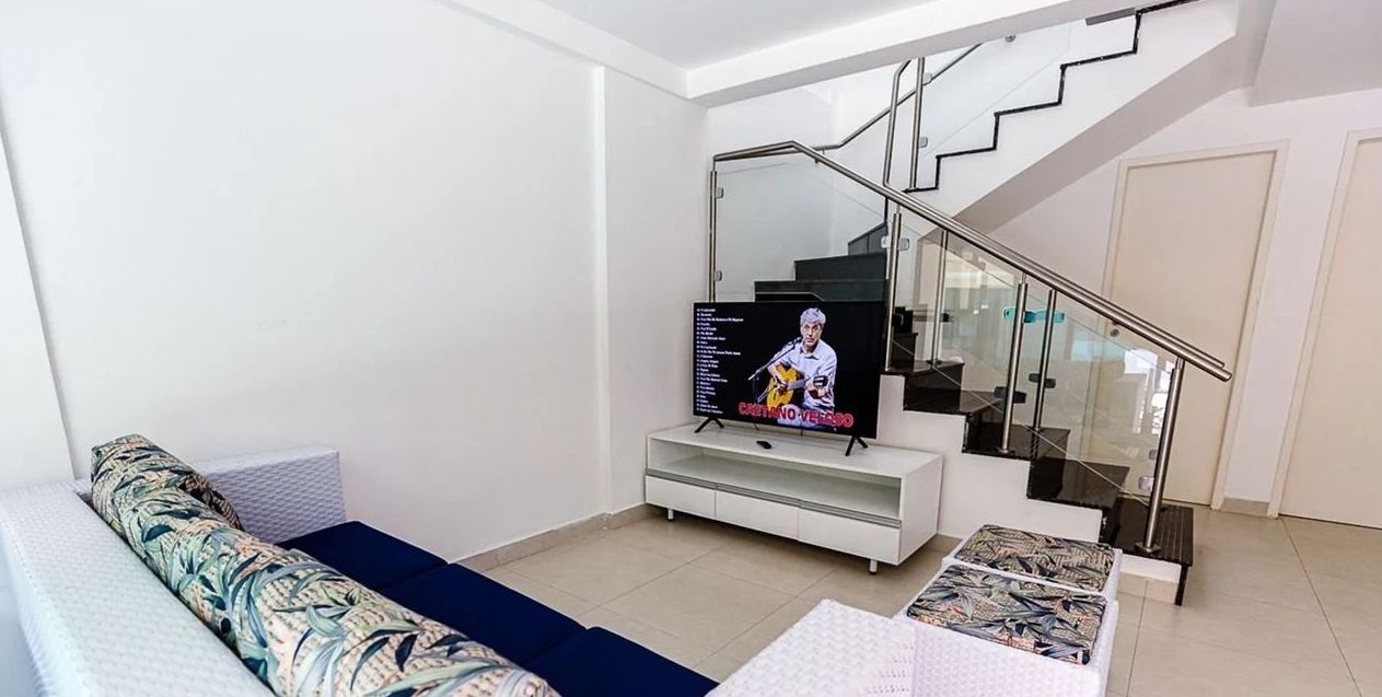 Een moderne woonkamer met een bank, een salontafel, een televisie en een trap met glazen leuning.