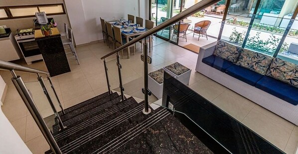 A modern interior with a staircase, a dining area, and a sofa with a view. - Beira Mar C Piscina e Area Gourmet 113D (Ipojuca)