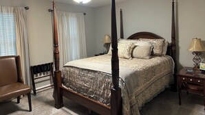 A four-poster bed with a canopy, a wooden chair, a nightstand with a lamp, and a radiator.