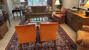 A living room with a sofa, two armchairs, a coffee table, a sideboard, and a window with curtains.