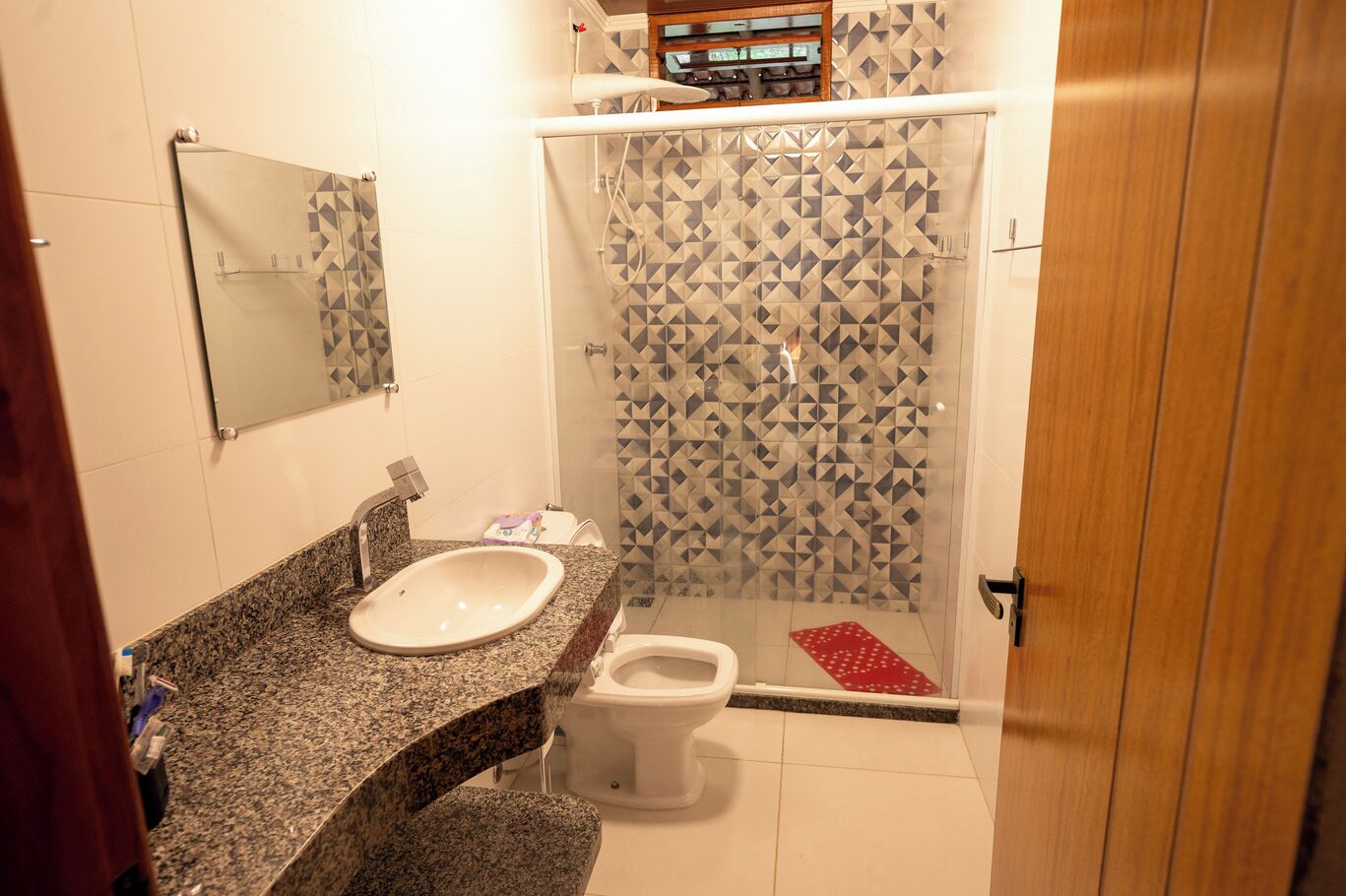 Un bagno con lavabo su piano in granito, un water e una doccia con decorazione a mosaico geometrico.