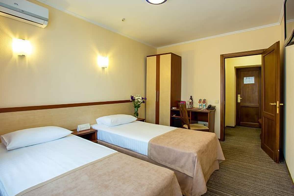 A hotel room with two beds, a desk, a chair, and a wardrobe.