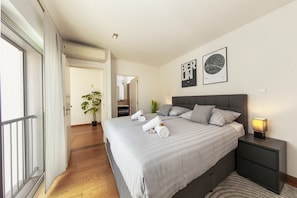 A modern bedroom with a large bed, bedside tables, and a view of the hallway. - Villa Santa Rosa (Silves)