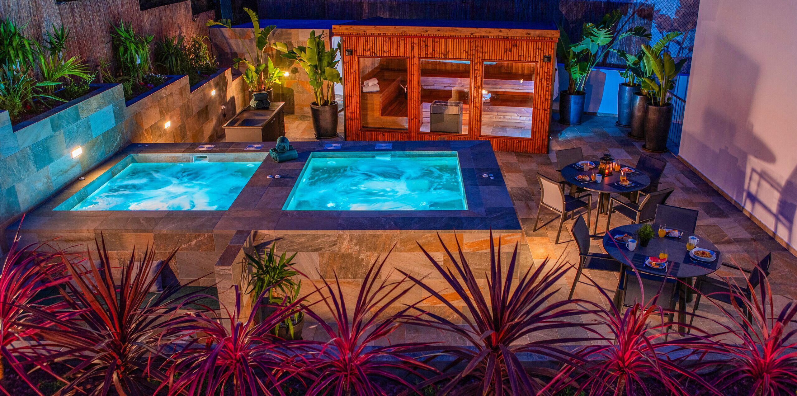 A spa area with two hot tubs, a wooden sauna, and a dining table with chairs.