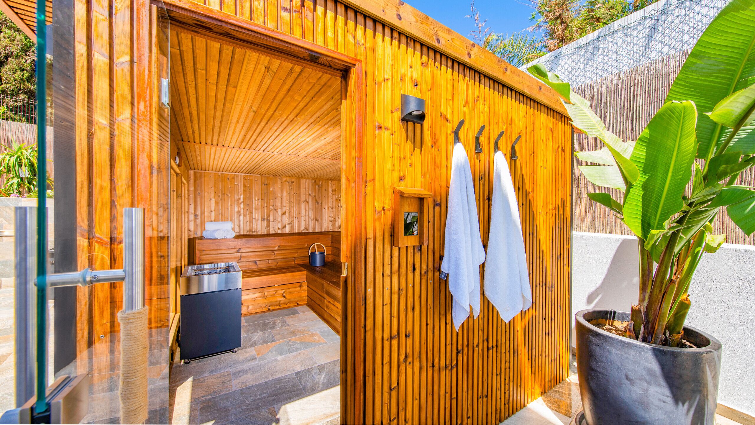 A wooden sauna with a bench, towels, and a small table with a bucket.