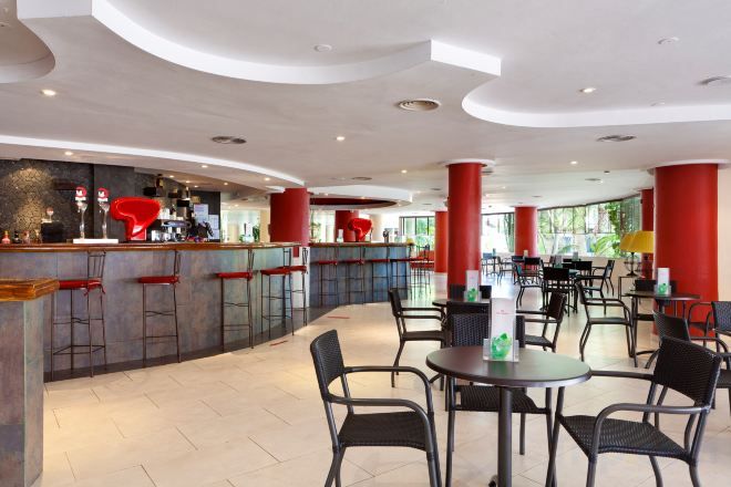 Un bar moderno con taburetes y una barra, rodeado de mesas y sillas en un espacio interior amplio.