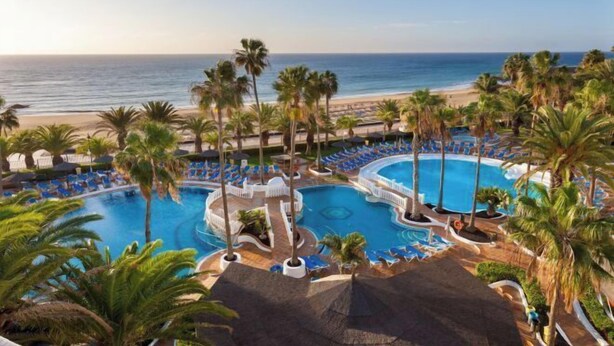 A resort with a large pool area, palm trees, and a beach view. - Sol Lanzarote All Inclusive (Puerto del Carmen)