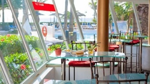 A glass-enclosed dining area with tables and chairs, overlooking a pool and outdoor seating area. - Sol Lanzarote All Inclusive (Puerto del Carmen)