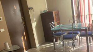 Ein Zimmer mit Esstisch und Stühlen, einem kleinen Beistelltisch mit Lampe, einem Schrank und einer Tür.
