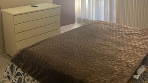 Ein Schlafzimmer mit einem Bett, einem Schminktisch, einem an der Wand montierten Fernseher und einem Fenster mit Vorhängen.