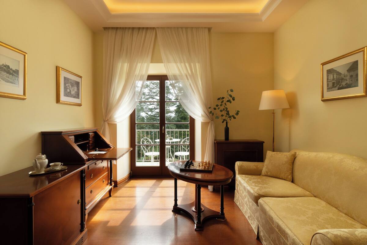 Una habitación con escritorio de madera, sofá, lámpara y ventana con cortinas.