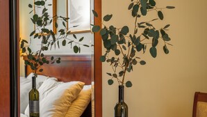 A room with a round wooden table, a mirror reflecting a bed and a chair, and two vases with green plants. - Dvorec Jeruzalem (Ljutomer)