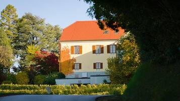 A two-story building with a red roof and white walls, surrounded by well-maintained gardens and trees.