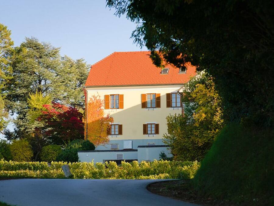 Un edificio de dos pisos con techo rojo y paredes blancas, rodeado de jardines y árboles bien cuidados.
