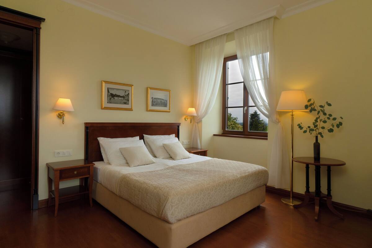 Una cama bien hecha con cabecera de madera, dos mesitas de noche con lámparas y dos cuadros enmarcados en la pared.
