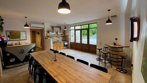 A modern kitchen with a long wooden table, bar stools, pendant lighting, and a view through large windows. - Rustic stone house-Casa Tilia-with pool and sauna, in peaceful village near sea. (Crno)