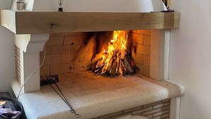 A fireplace with a wooden mantel, a brick interior, and a hanging light fixture. - Rustic stone house-Casa Tilia-with pool and sauna, in peaceful village near sea. (Crno)