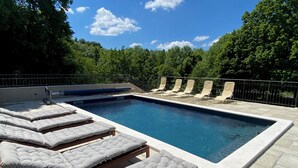 A rectangular swimming pool with lounge chairs and a spa chair, surrounded by a stone deck and trees. - Rustic stone house-Casa Tilia-with pool and sauna, in peaceful village near sea. (Crno)