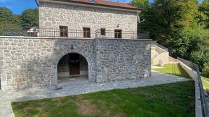 A stone building with a central archway, a balcony, and a staircase leading to an upper level. - Rustic stone house-Casa Tilia-with pool and sauna, in peaceful village near sea. (Crno)