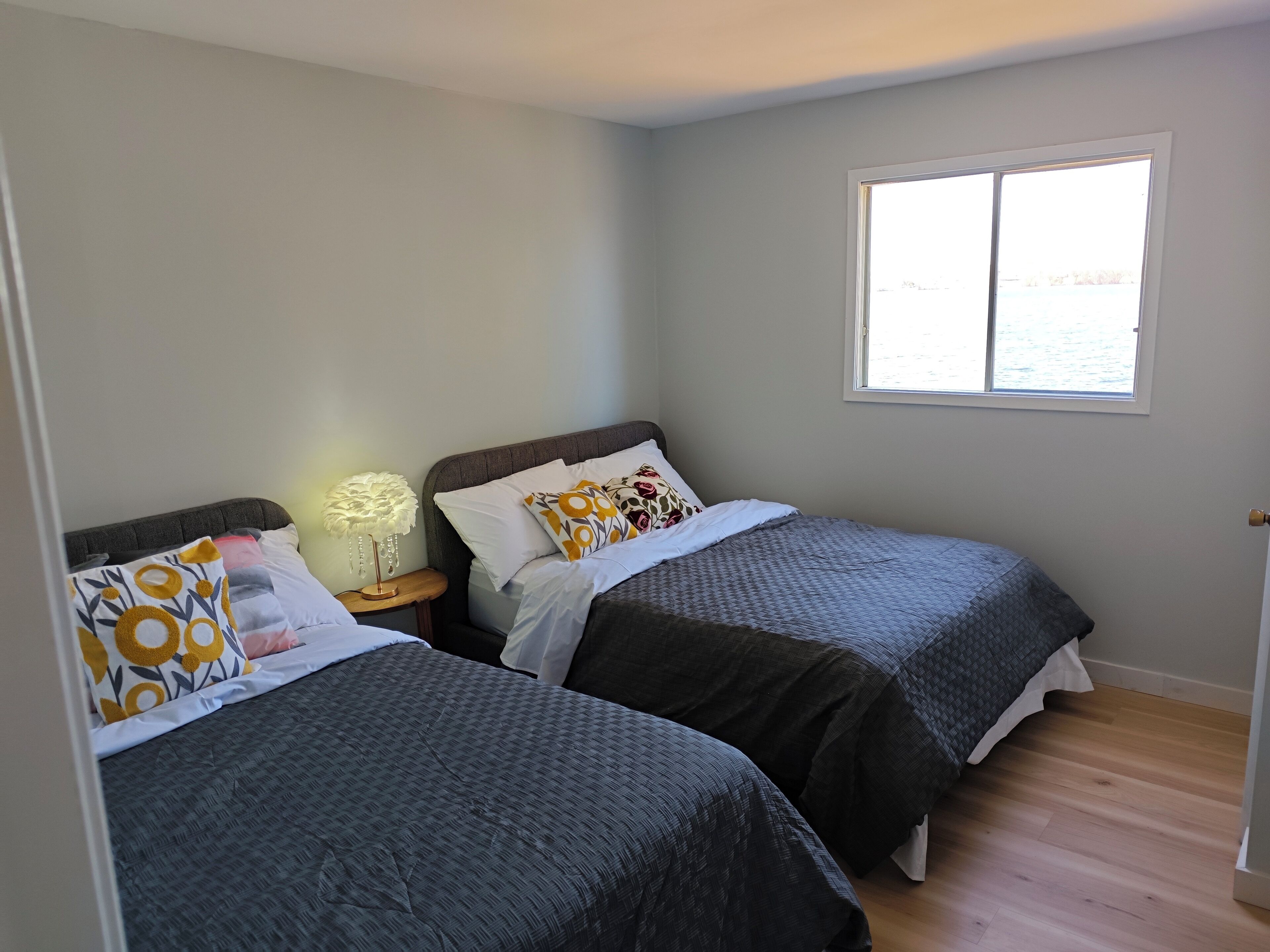 A bedroom with two beds, a nightstand with a lamp, and a window with a view of the water.