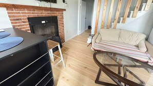 Ein Wohnzimmer mit Kamin aus Ziegelsteinen, einer Couch, einem Glastisch und einem an der Wand befestigten Fernseher.
