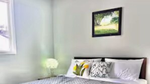 Ein Schlafzimmer mit Bett, Nachttisch, Fenster und einem gerahmten Bild an der Wand.